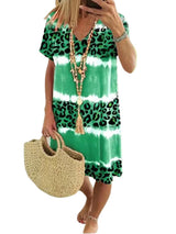 Woman wearing a green tie-dye and leopard print short-sleeve V-neck A-line dress, holding a straw bag, with a white background.