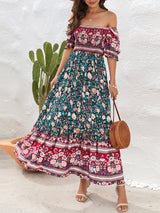 Woman wearing a floral print off-the-shoulder maxi dress with puff sleeves and a tiered skirt, holding a straw bag, with a cactus in the background.