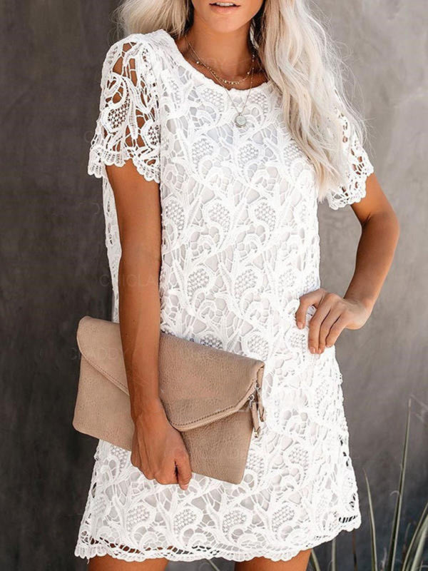 woman wearing a white lace mini dress with short sleeves and a round neckline, holding a beige clutch