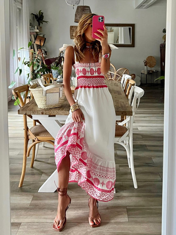 Woman wearing a white and pink embroidered maxi dress, lifting the hem to show the details.