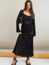 Woman wearing a black crochet knit maxi dress with long sleeves and a square neckline, holding a black handbag.