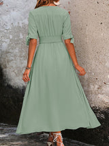 Back view of a woman wearing a sage green A-line maxi dress with a smocked waist and tie sleeves.