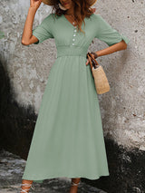 Woman wearing a sage green A-line maxi dress with a smocked waist and tie sleeves, holding a straw bag.