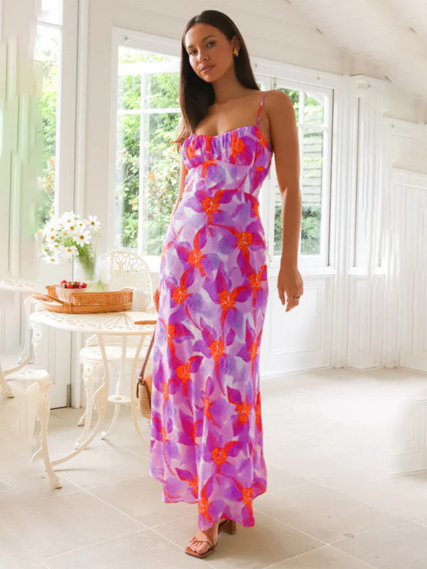 Woman wearing a purple and orange floral print maxi dress with spaghetti straps and a ruched bust, standing indoors.