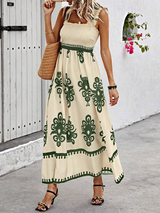 Woman wearing a cream and green floral print maxi dress with smocked bodice and square neckline, standing on a cobblestone path.