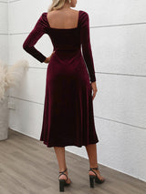 Back view of a woman wearing a long-sleeved, wine-colored velvet midi dress with a sweetheart neckline and a high slit.