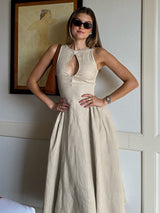 Woman wearing a beige sleeveless A-line dress with a keyhole neckline and a pleated skirt, accessorized with sunglasses and a brown shoulder bag.