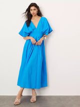 Woman wearing a vibrant blue V-neck dolman sleeve midi dress with a pleated A-line skirt, silver strappy heels, and silver jewelry.