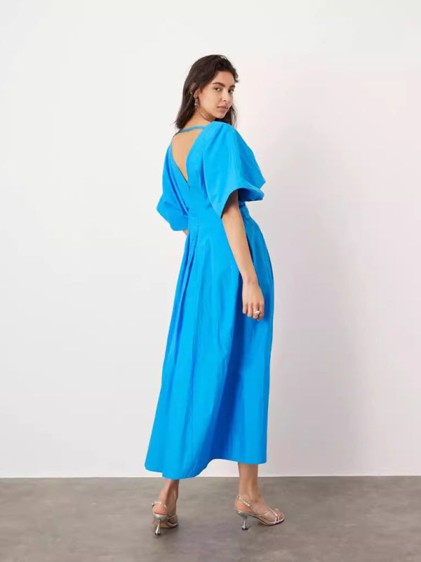 Woman from behind wearing a vibrant blue V-neck dolman sleeve midi dress with a pleated A-line skirt and silver strappy heels.