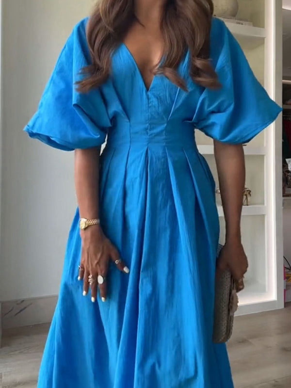 Close-up of a woman wearing a vibrant blue V-neck dolman sleeve midi dress with a pleated skirt, accessorized with a watch and rings.