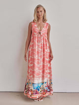 Woman wearing a pink sleeveless maxi dress with a cloud print and a scenic border.
