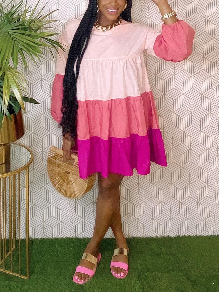 Woman wearing a pink and purple tiered dress, gold chain necklace, and bamboo handbag with gold sandals.