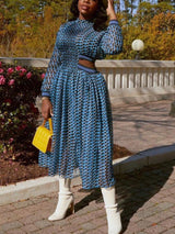 Woman wearing a blue and black geometric print midi dress with cut-out details and long sleeves, paired with white boots and a yellow handbag.