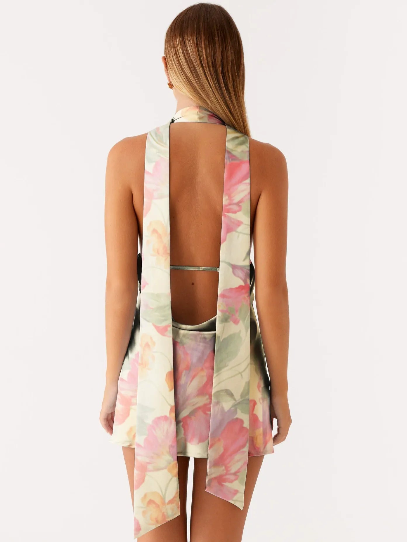 Back view of a woman in a pink floral print mini dress showing the open back and scarf detail