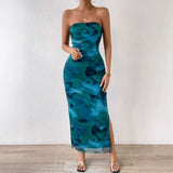 Woman standing, showing the front of a strapless blue and green abstract floral print maxi dress with a high slit.