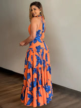 Woman wearing a teal and red tropical print maxi dress with a high slit and one-shoulder design.