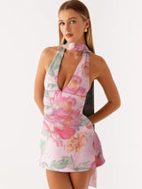 Woman wearing a pink floral print mini dress with a halter neckline and open back