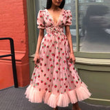 Woman wearing a light pink midi dress with a strawberry print, puff sleeves, and a ruffled hem outdoors.