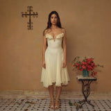 Woman standing in a pale yellow, A-line, calf-length dress with floral bodice details and a ruffled hem. She is wearing strappy heels.