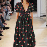 Woman wearing a black midi dress with a strawberry print and puff sleeves on a runway.