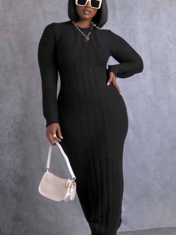Woman wearing a long black cable knit dress with long sleeves and a mock neck, holding a white handbag.
