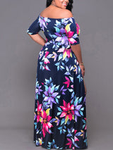 Back view of a woman in a navy blue floral print off-the-shoulder maxi dress with a high leg slit.