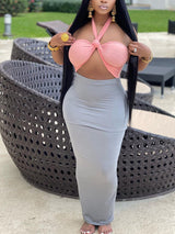 Woman wearing a light pink halter crop top with a knot detail and a grey maxi skirt.