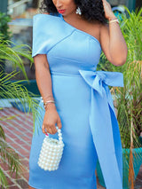 Close-up of a woman in a light blue one-shoulder midi dress with a bow detail, accessorized with bracelets and a pearl handbag.