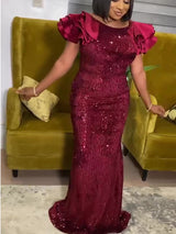 Woman in a burgundy sequined mermaid dress with ruffled sleeves, posing with arms slightly outstretched.