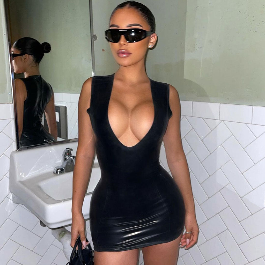 Woman in a black glossy sleeveless mini dress with a deep V-neckline standing in front of a mirror