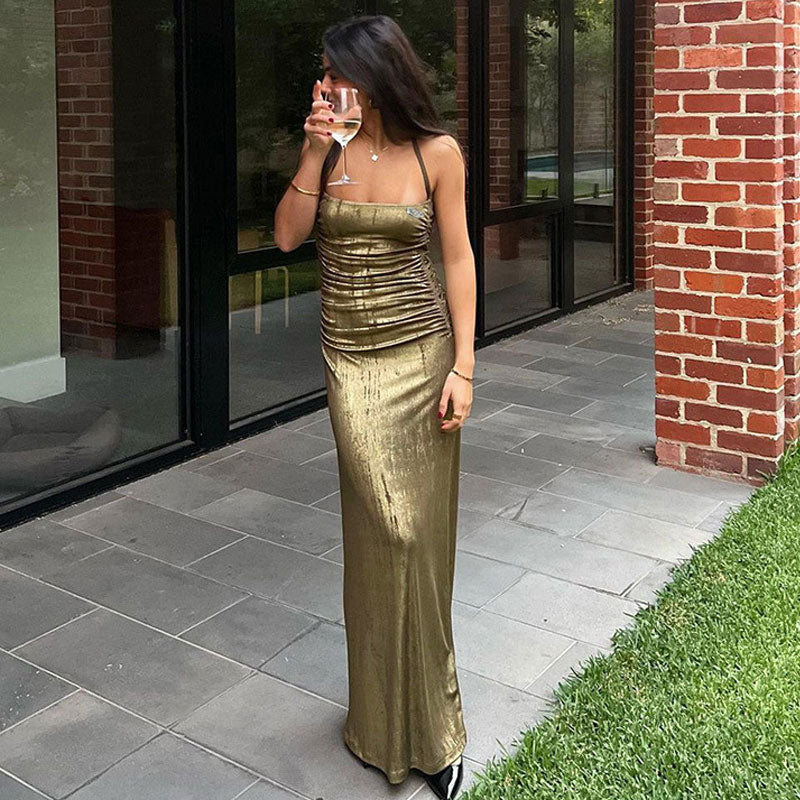 Woman wearing a shimmering gold maxi dress holding a glass of wine outdoors.