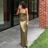 Woman wearing a shimmering gold maxi dress holding a glass of wine outdoors.