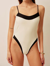 Front view of a woman wearing a cream and black colorblock one-piece swimsuit