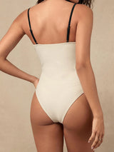Back view of a woman wearing a cream and black colorblock one-piece swimsuit