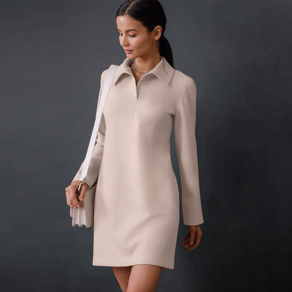Woman wearing a light beige long-sleeved collared shift dress and carrying a white handbag.