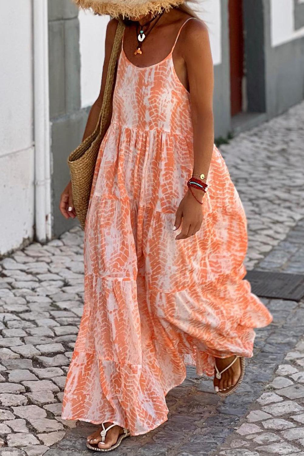 Woman wearing an orange and white tie-dye maxi dress with spaghetti straps and a tiered skirt, carrying a straw tote bag.