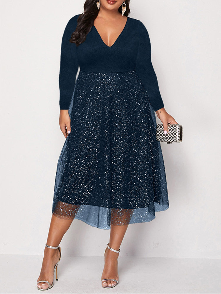 Woman wearing a navy blue long-sleeved V-neck midi dress with sparkly embellishments and a tulle overlay, paired with silver heels and a clutch.