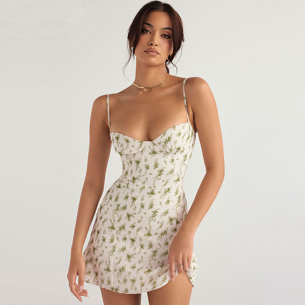 Woman wearing a white mini dress with a green floral print and spaghetti straps.