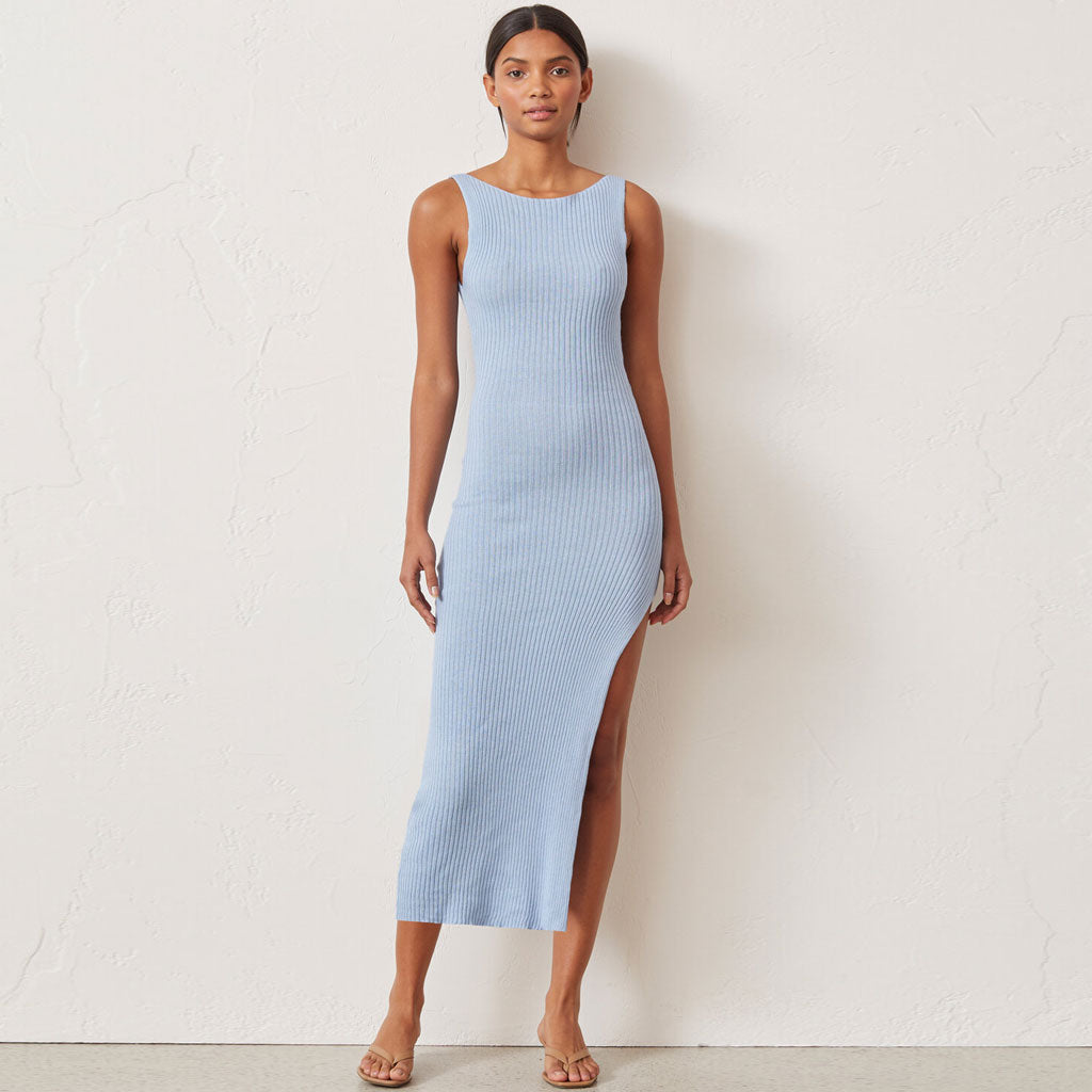 woman wearing a light blue ribbed knit sleeveless midi dress with a high slit standing against a stone wall