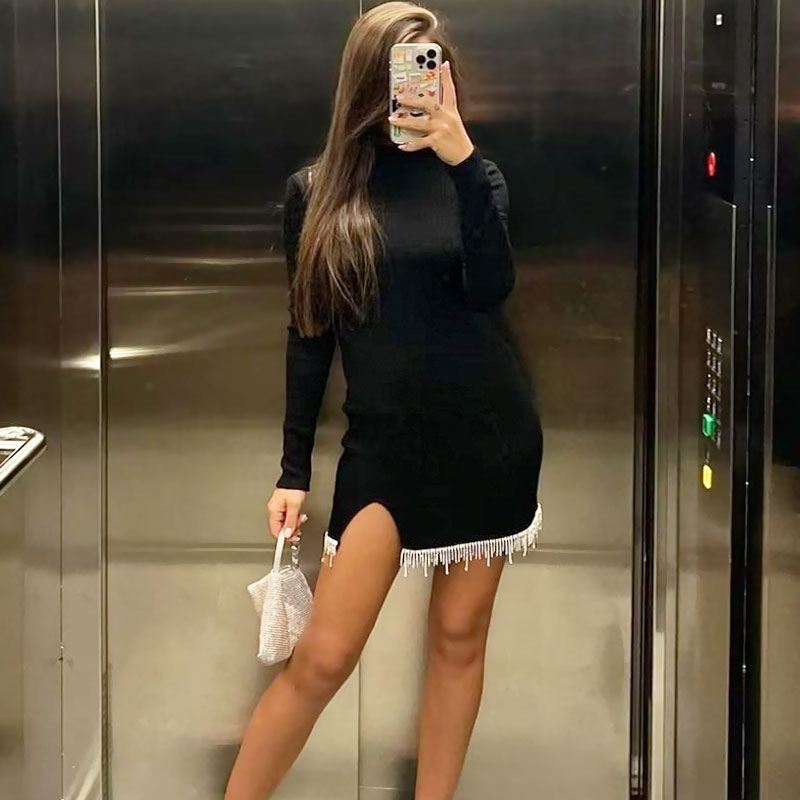 woman in black dress with beaded trim and side slit posing in an elevator