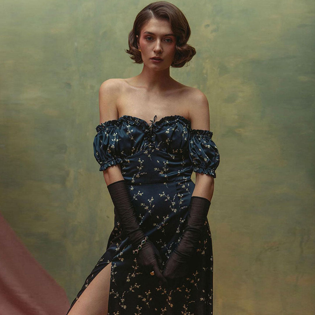 Woman wearing a dark blue floral print off-the-shoulder dress with puff sleeves and a high slit, paired with long sheer gloves.