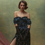 Woman wearing a dark blue floral print off-the-shoulder dress with puff sleeves and a high slit, paired with long sheer gloves.