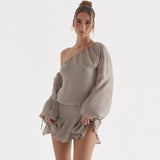 Front view of a woman in a grey one-shoulder dress with flowing sleeves and a short, ruffled hem.