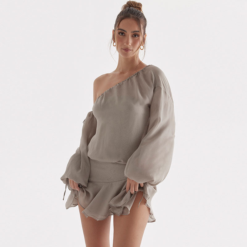 Front view of a woman in a grey one-shoulder dress with flowing sleeves and a short, ruffled hem.