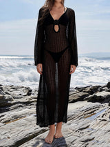 Woman wearing a black crochet maxi dress over a black bikini, standing on rocks by the ocean.