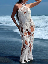 Woman wearing a white crocheted maxi dress with cut-out details on a beach.