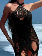 Close-up of a woman wearing a black crocheted maxi dress with cut-out details on a beach.