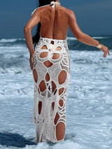 Back view of a woman wearing a white crocheted maxi dress with cut-out details in the ocean.