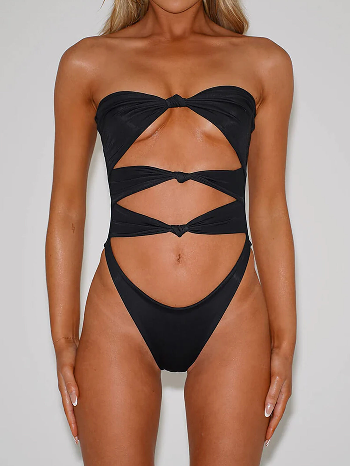 Woman wearing a black strapless one-piece swimsuit with cut-outs and a twisted front