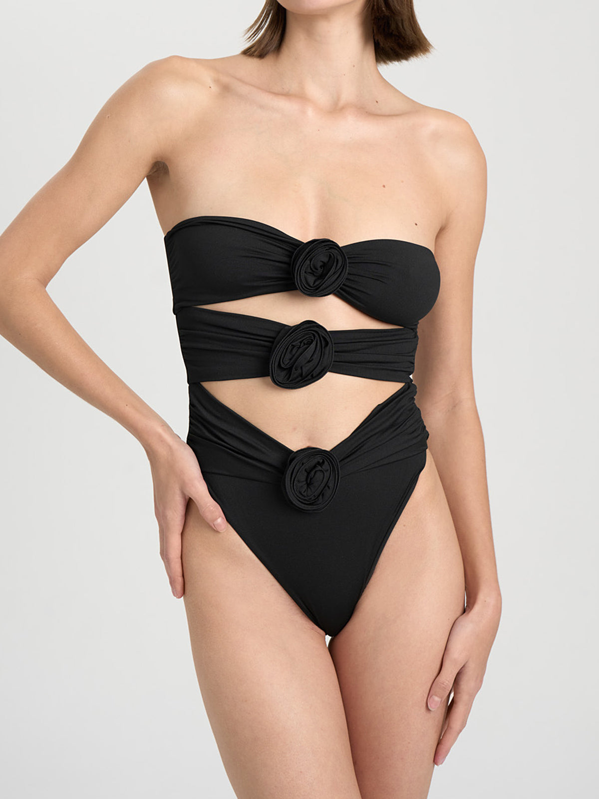 Front view of a black strapless one-piece swimsuit with cut-out details and floral embellishments.